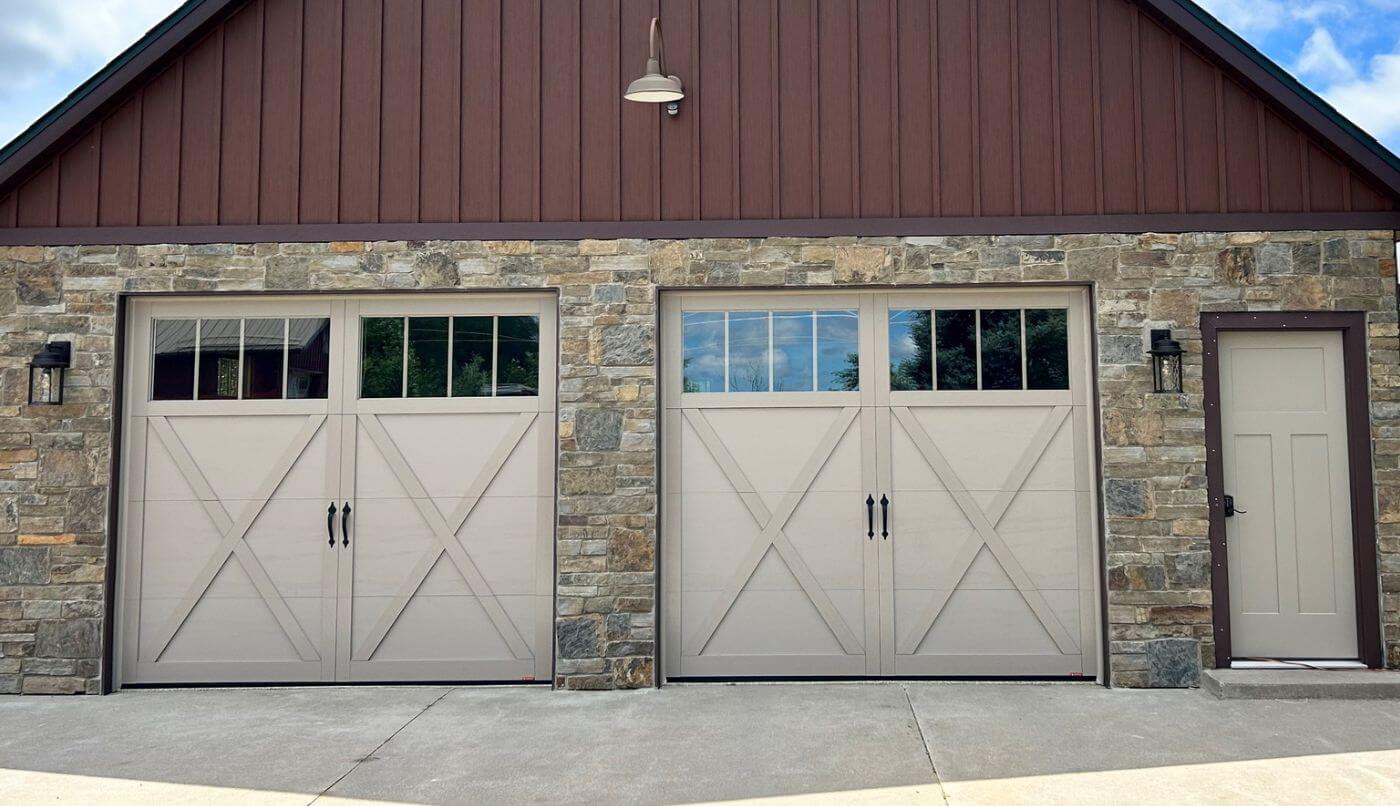 Two garage doors featuring windows, set against a textured stone wall, creating a harmonious architectural design.